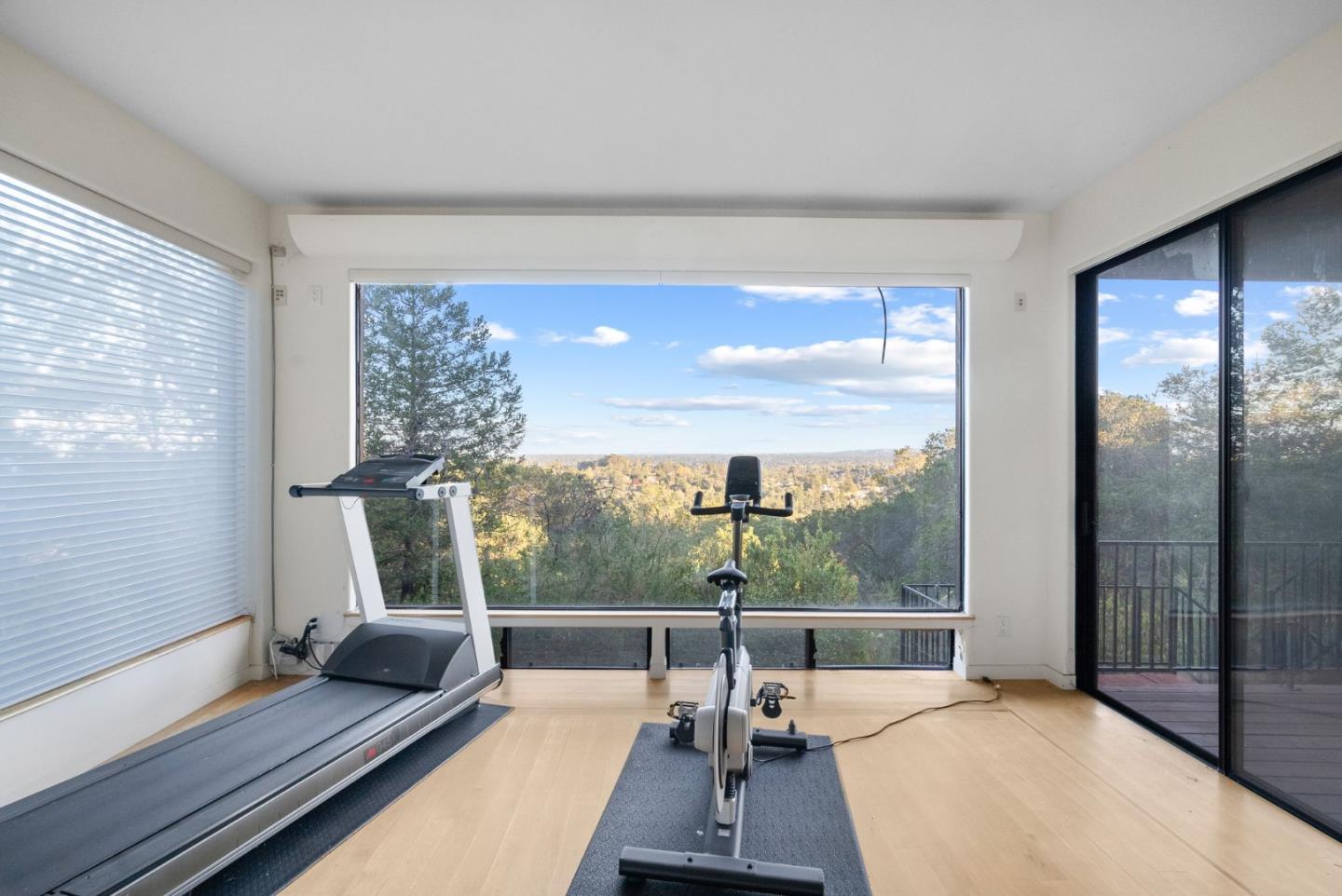 Home gym with treadmill and stationary bike overlooking autumn trees and distant hills.