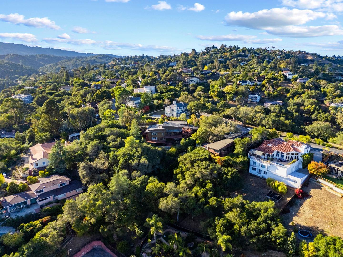 Aerial view of a wooded hillside neighborhood with homes and distant green hills.