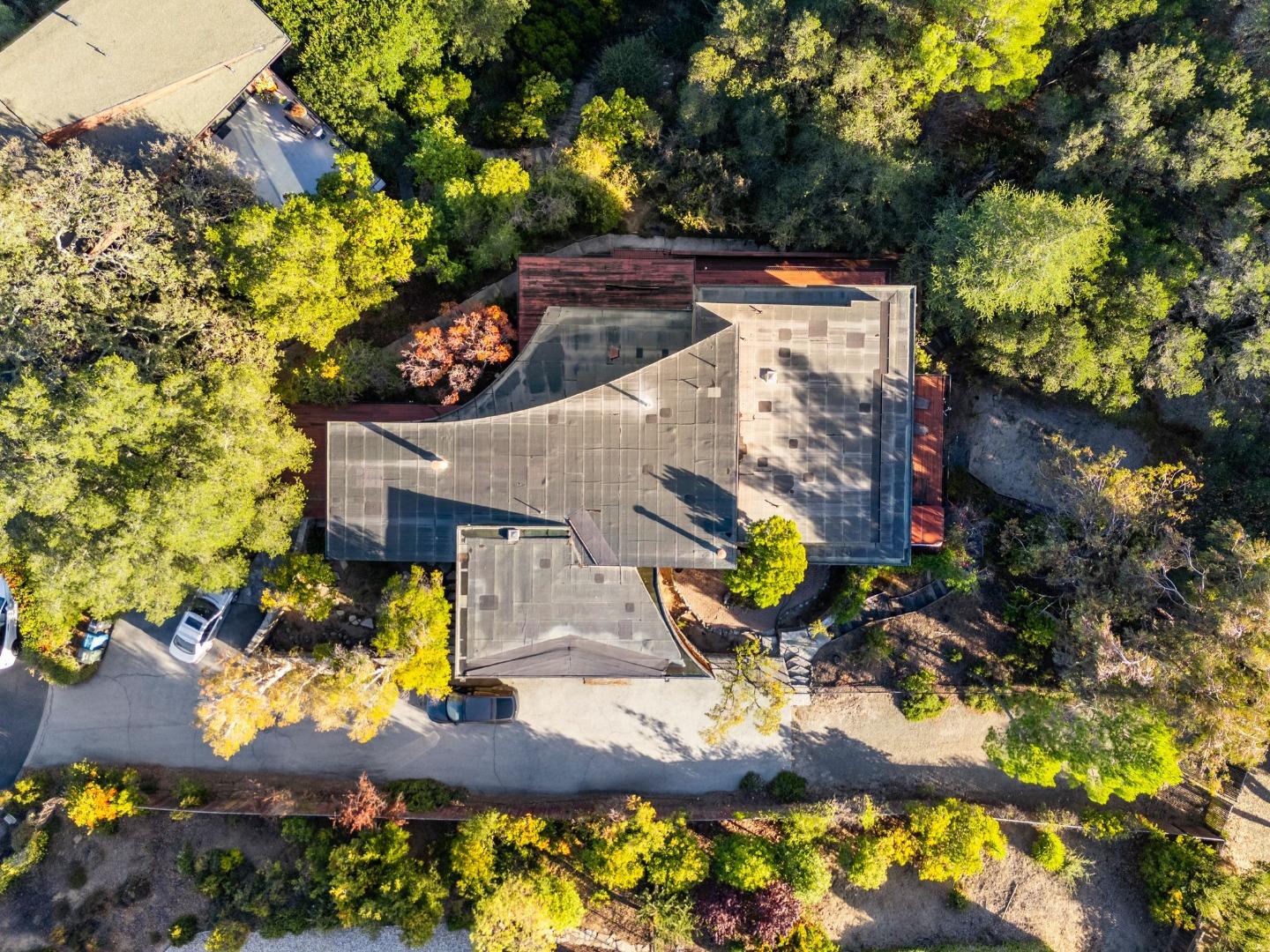 Aerial view of a home with a broad roof, mature trees, and a curved driveway.