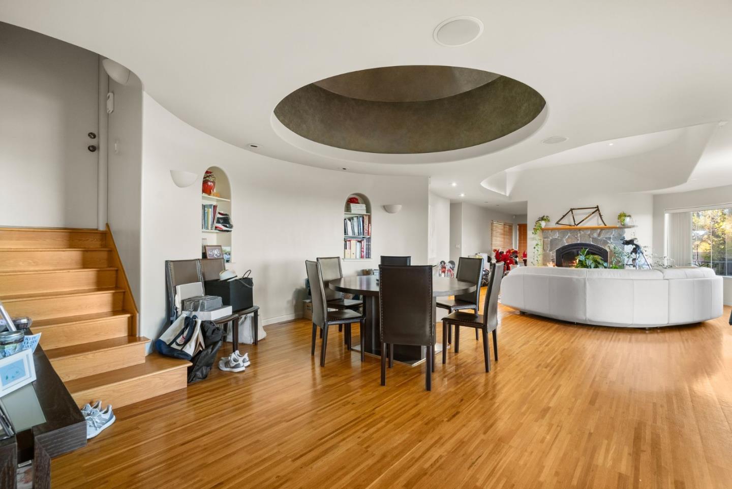 Open-plan dining and living room with hardwood floors, a stone fireplace, and a circular ceiling feature.