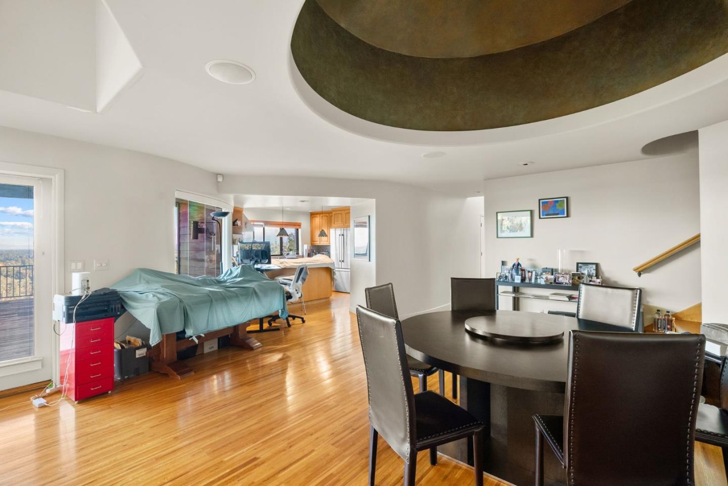 Dining area with a round dark table, hardwood floors, and an open view into the kitchen.