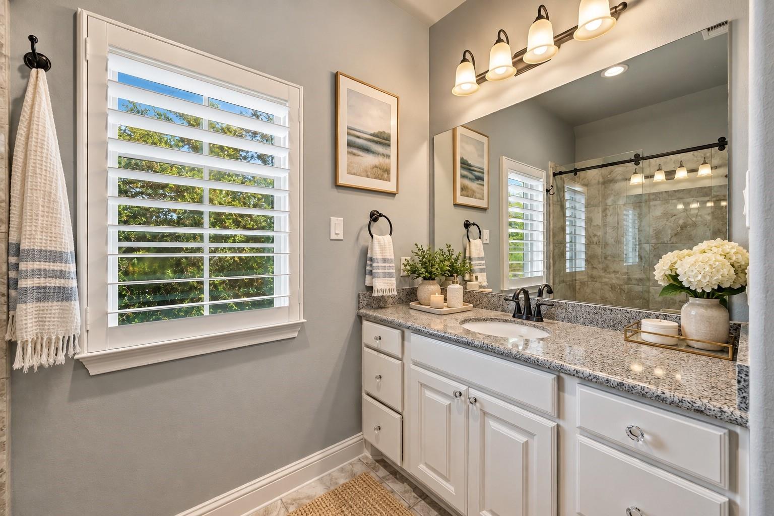Bright bathroom with white vanity, speckled stone countertop, shuttered windows, and glass-enclosed tiled shower.