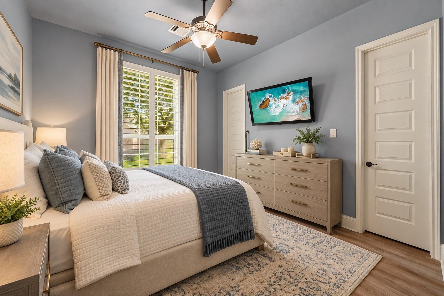 Bedroom with a neutral upholstered bed, gray accents, plantation shutters, and a light wood dresser.