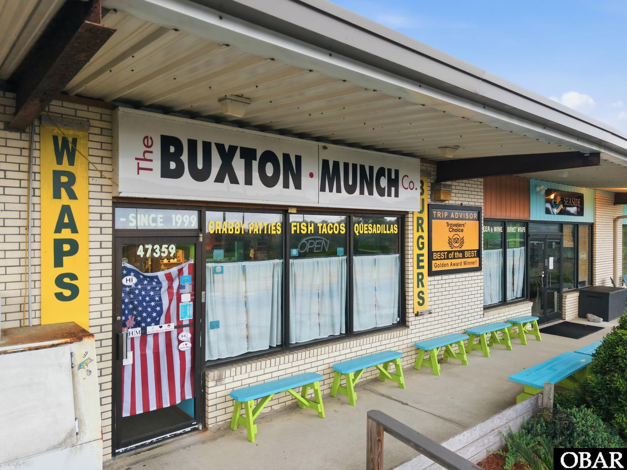 The Buxton Munch Co. storefront with yellow signs and turquoise-and-green picnic benches.