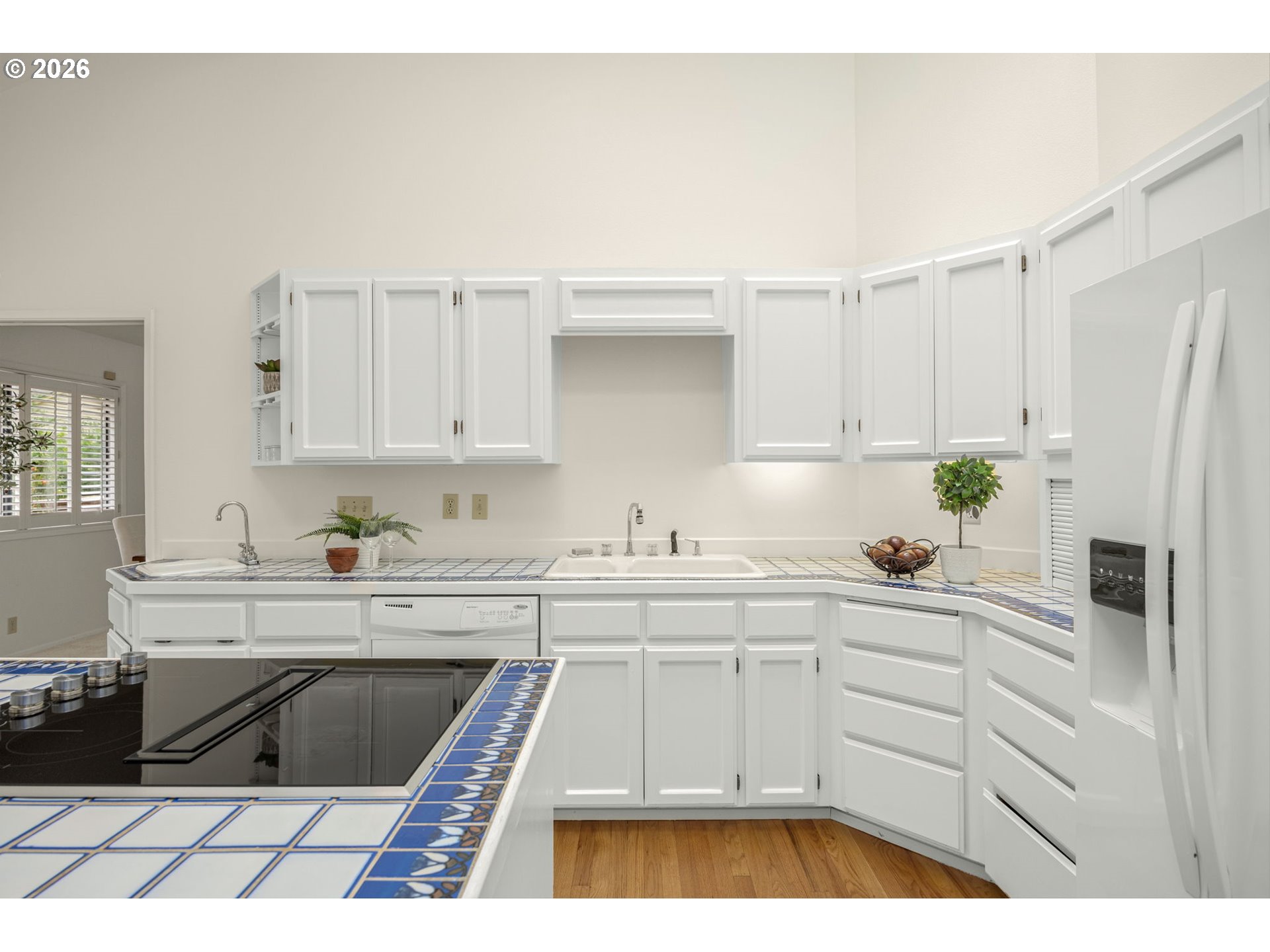 Kitchen with white cabinets, blue-accented tile counters, a black cooktop island, and hardwood floors.