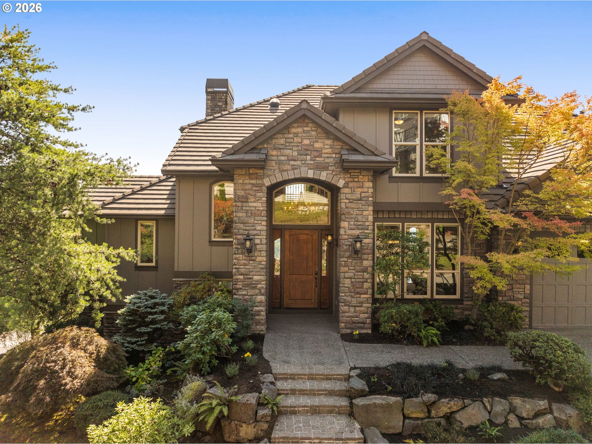 Two-story stone-front home with an arched entry and landscaped stone walkway.