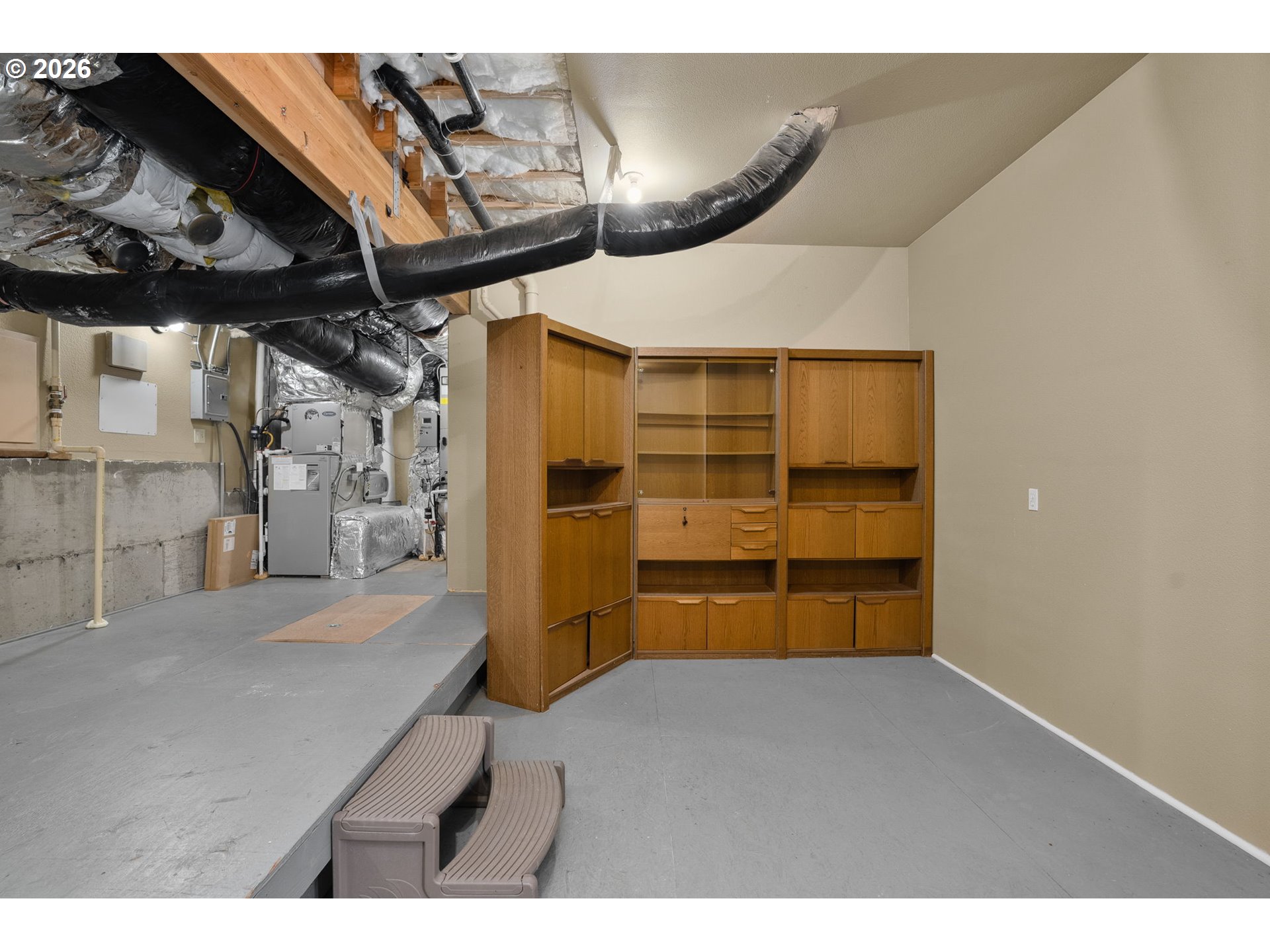 Basement storage area with built-in wooden shelving beneath exposed HVAC ducts.