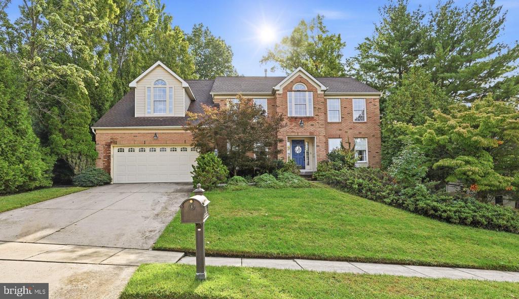 Two-story brick house with an attached garage, broad driveway, and mature trees.