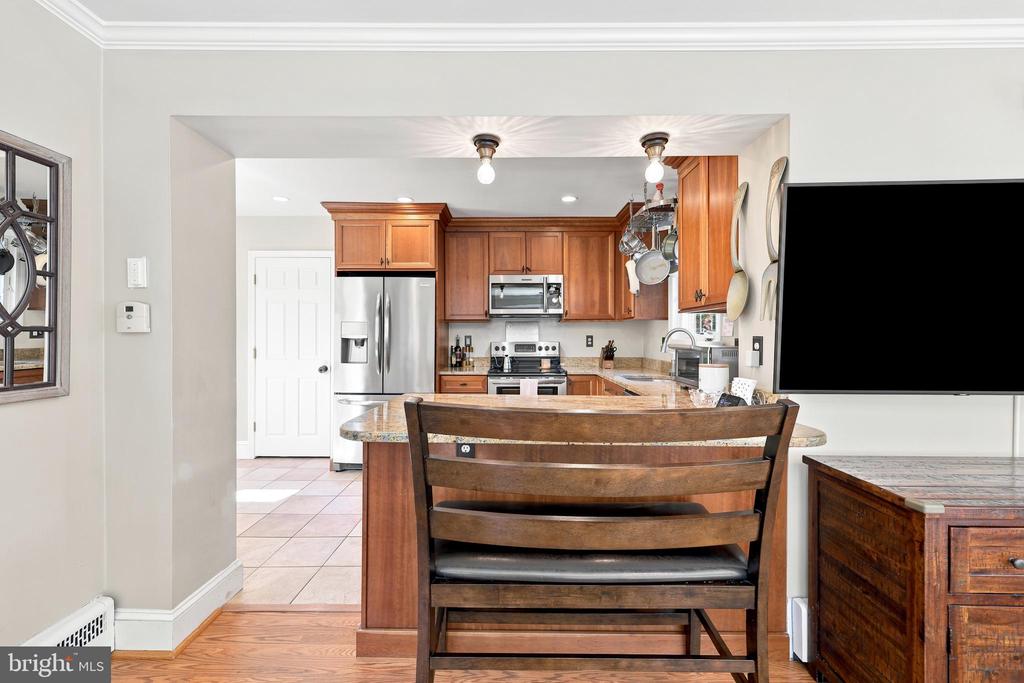 Kitchen with warm wood cabinets, stainless steel appliances, and a granite island with a wooden chair.