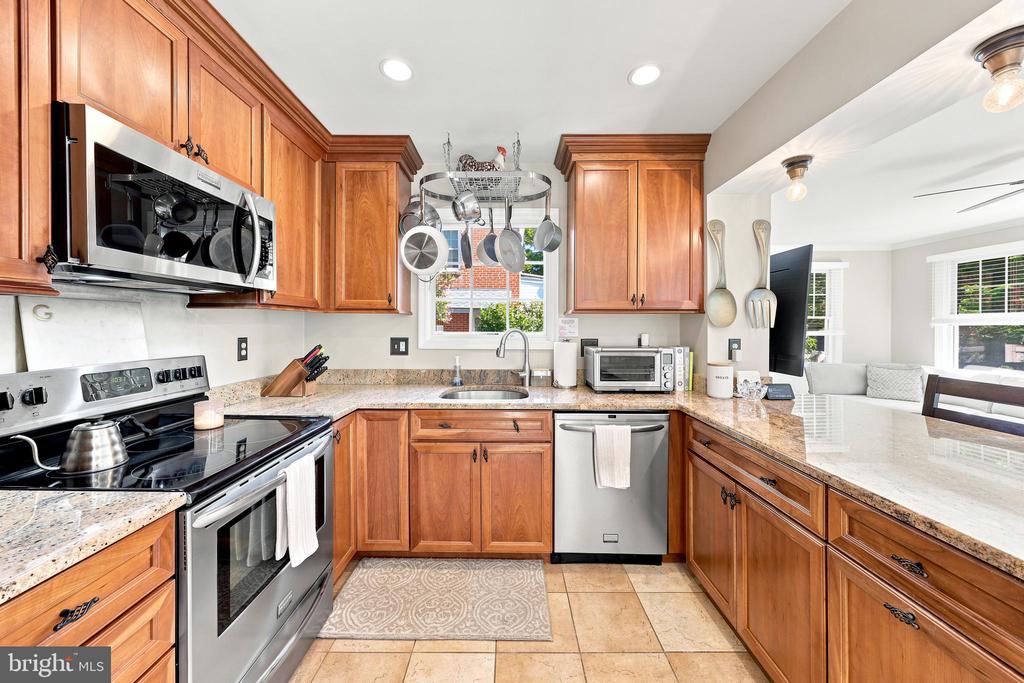 Kitchen with warm wood cabinets, granite counters, stainless steel appliances, and a hanging pot rack.