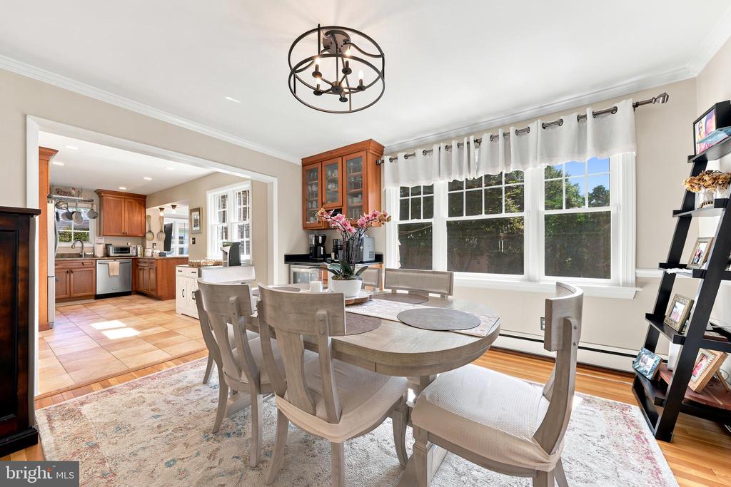 Dining room with a round table beside large windows and an open view into the wood-cabinet kitchen.