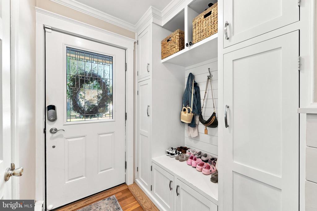 Entryway with a glass-paneled front door and built-in mudroom bench, cabinets, and hooks.