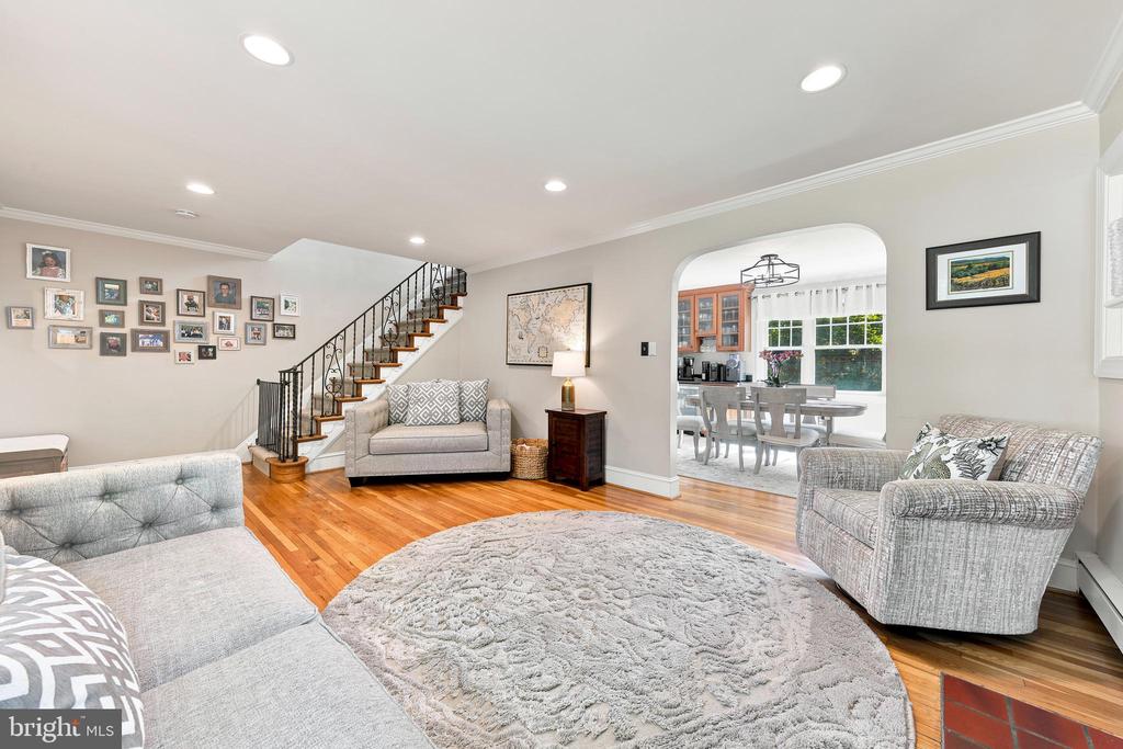 Living room with gray seating, a round rug, hardwood floors, and a staircase beside an arched dining-room opening.