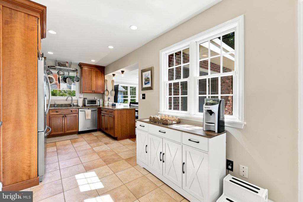 Kitchen with warm wood cabinetry, stainless steel appliances, and a white sideboard under a large window.