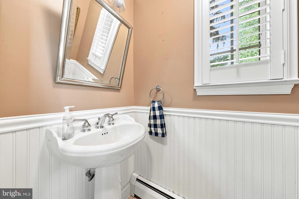 Bathroom with a white pedestal sink, beadboard wainscoting, and a shuttered window.