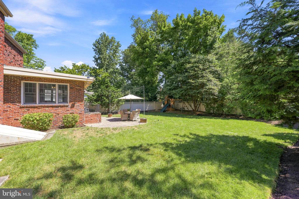 Backyard with a broad lawn, mature trees, and a patio beside the red brick house.