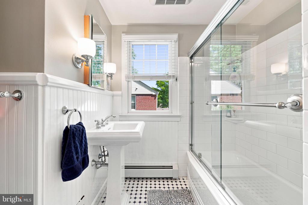 Bathroom with pedestal sink, glass-enclosed tub and shower, and black-and-white patterned tile floor.
