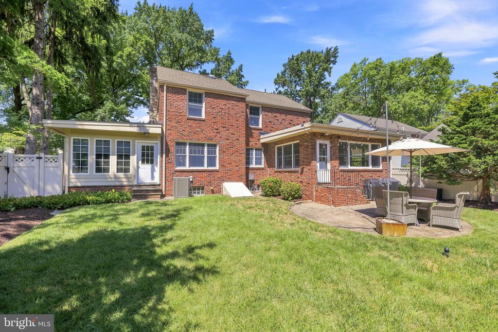 Brick home’s rear exterior with a broad lawn and patio seating under a white umbrella.