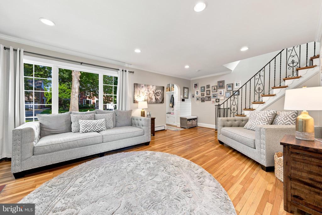 Living room with gray sofas, hardwood floors, large windows, and an ornate iron staircase.