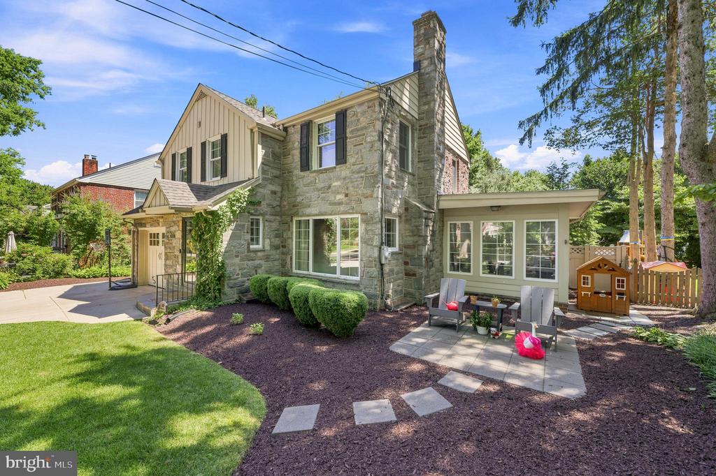 Rear of a stone home with a paved patio, outdoor seating, and landscaped yard.
