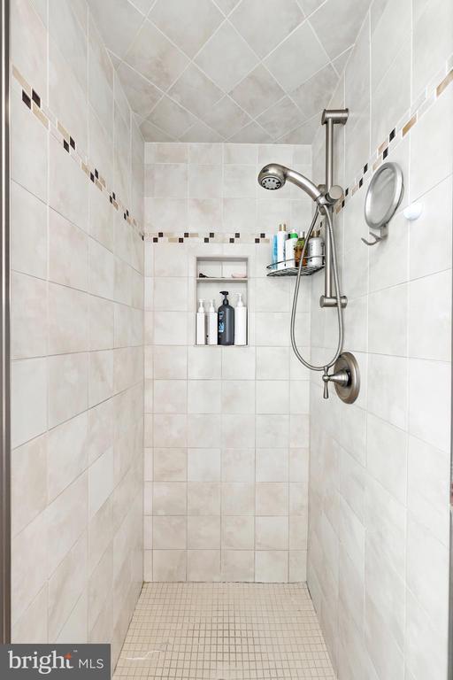 Walk-in shower with pale tile, recessed niches, and a handheld showerhead.