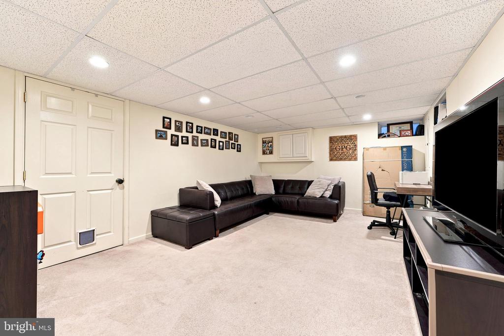 Finished basement lounge with a leather sectional, light carpet, and a large television.