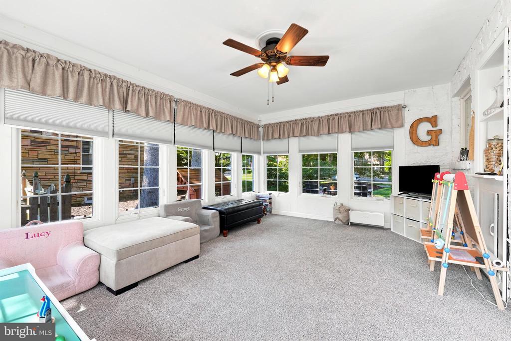 Bright sunroom with large windows, gray carpet, and a children’s play area.