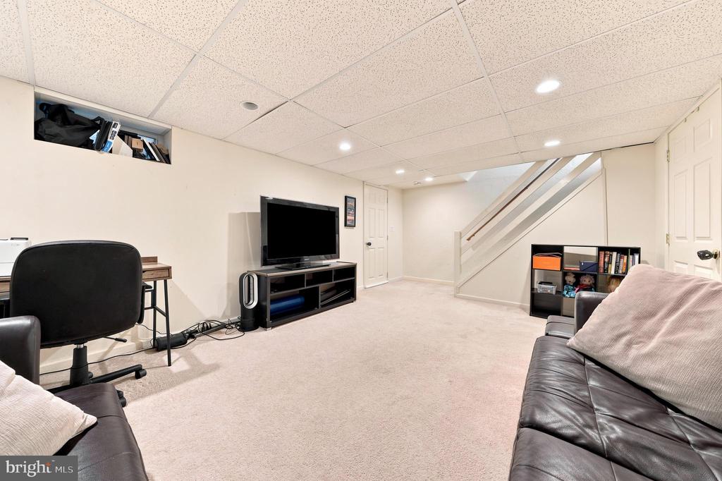 Furnished basement recreation room with a staircase, television, desk, and leather sofas.