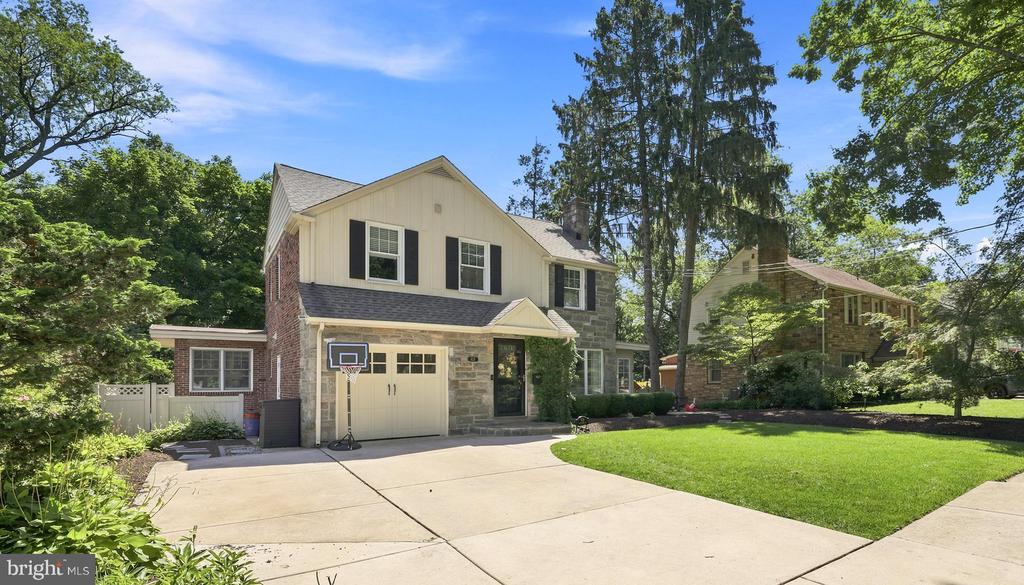 Two-story brick and stone home with an attached garage, basketball hoop, and broad driveway.