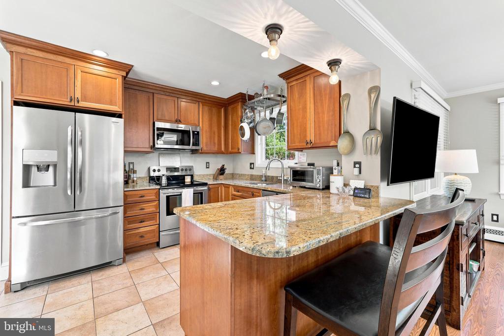 Kitchen with warm wood cabinets, stainless steel appliances, and a granite island with bar stools.