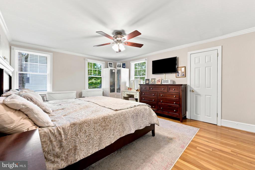 Bedroom with a large patterned bed, dark wood dresser, hardwood floors, and ceiling fan.