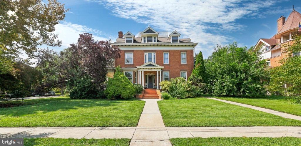 Two-story brick home with a columned porch, central walkway, and broad green lawn.