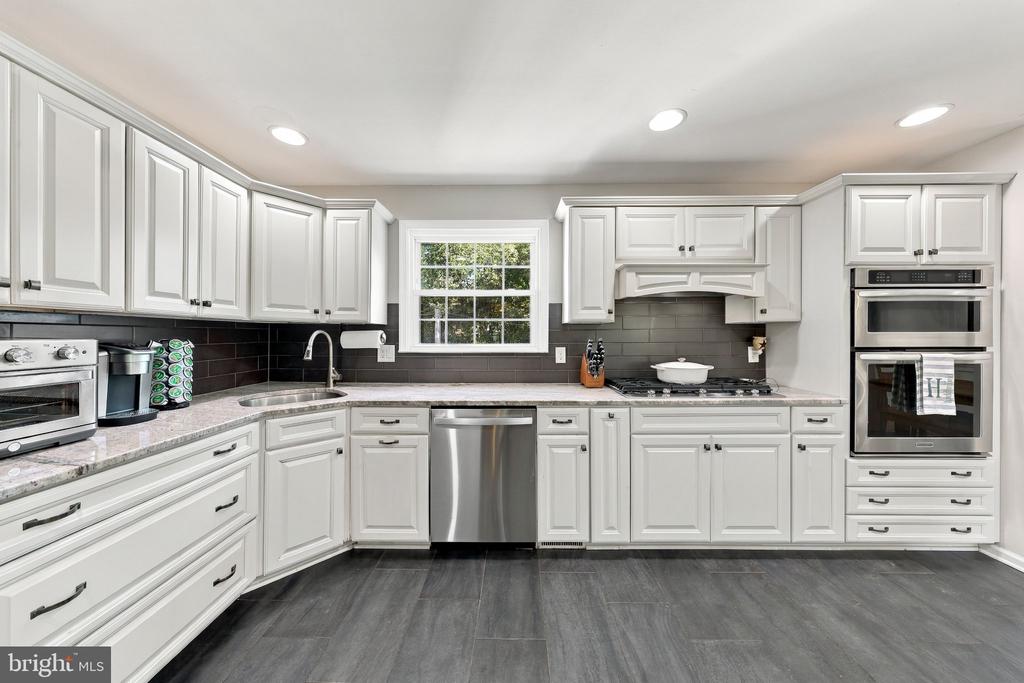 Bright kitchen with white cabinetry, dark tile backsplash, stainless appliances, and gray flooring.
