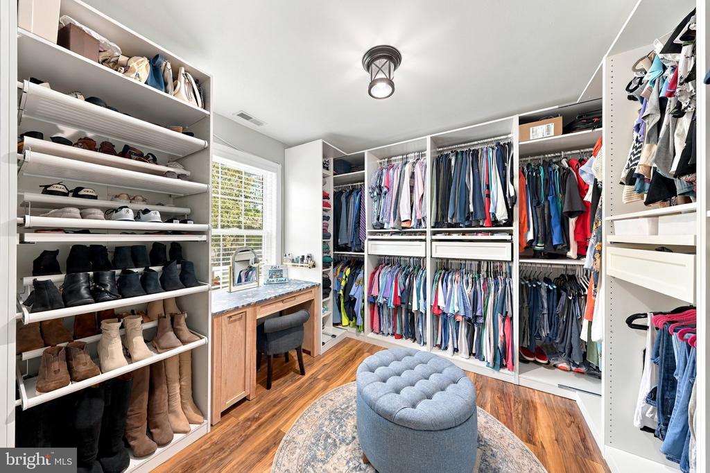 Walk-in closet with extensive clothing and shoe storage, a vanity, and a tufted ottoman.