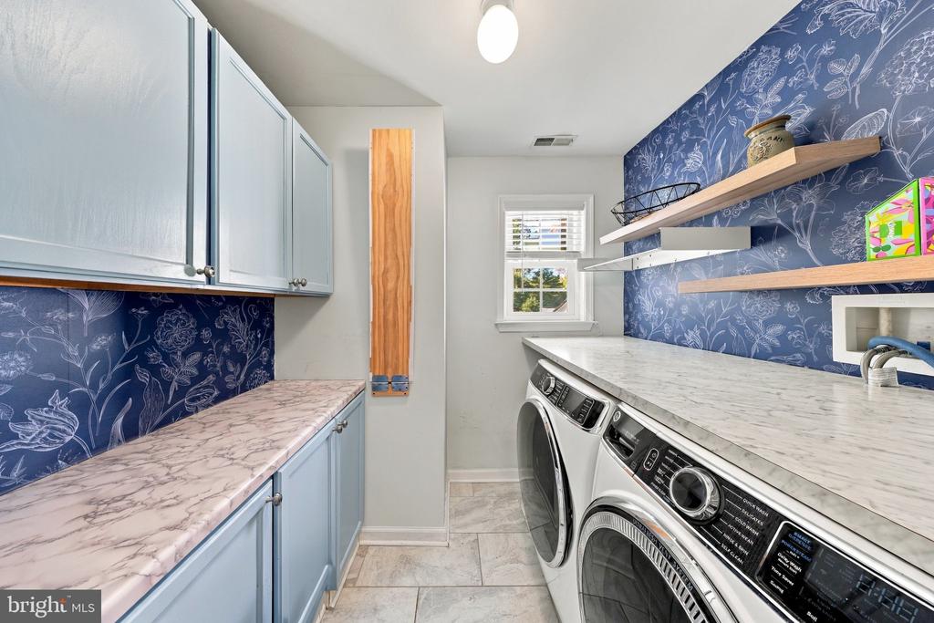 Laundry room with front-loading washer and dryer, blue cabinetry, and floral wallpaper.