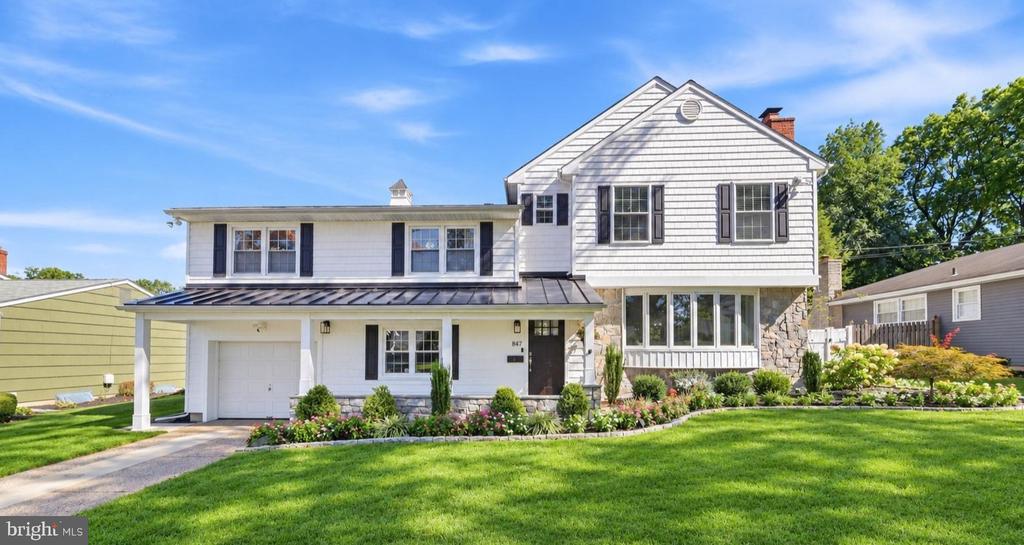 White two-story home with an attached garage, dark roof, and landscaped front lawn.