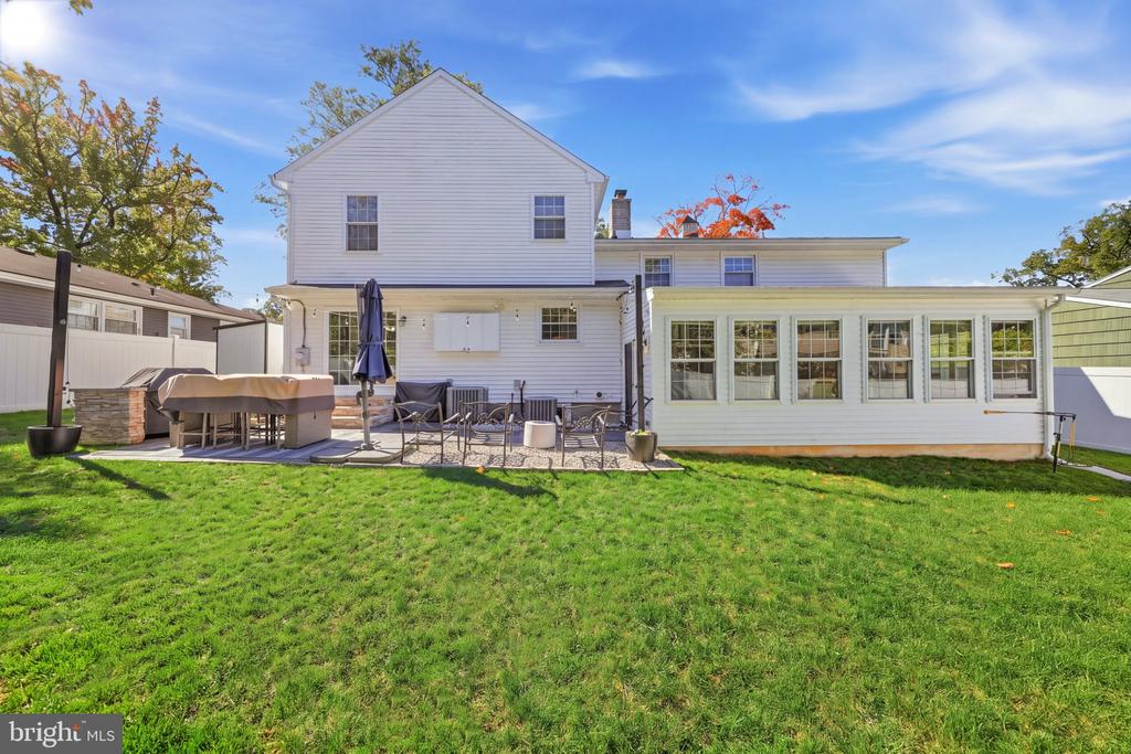 Rear of a white two-story home with an enclosed sunroom, patio seating, and a broad green lawn.