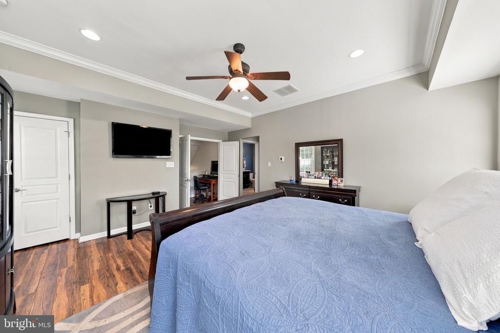 Bedroom with a blue quilted bedspread, ceiling fan, and hardwood flooring.
