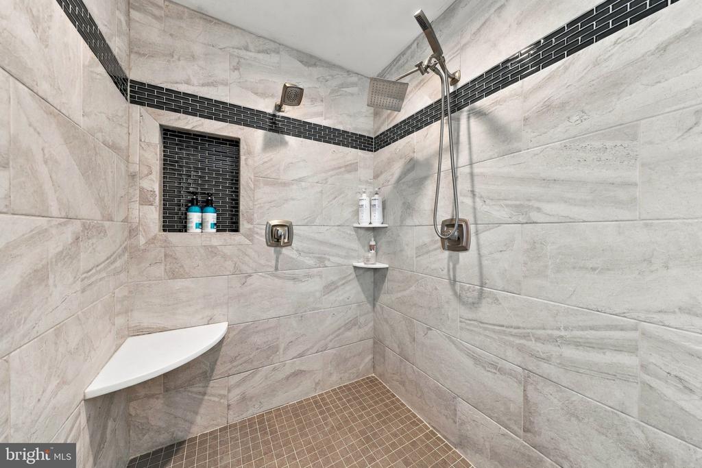 Tiled walk-in shower with multiple showerheads, a recessed niche, and a corner bench.