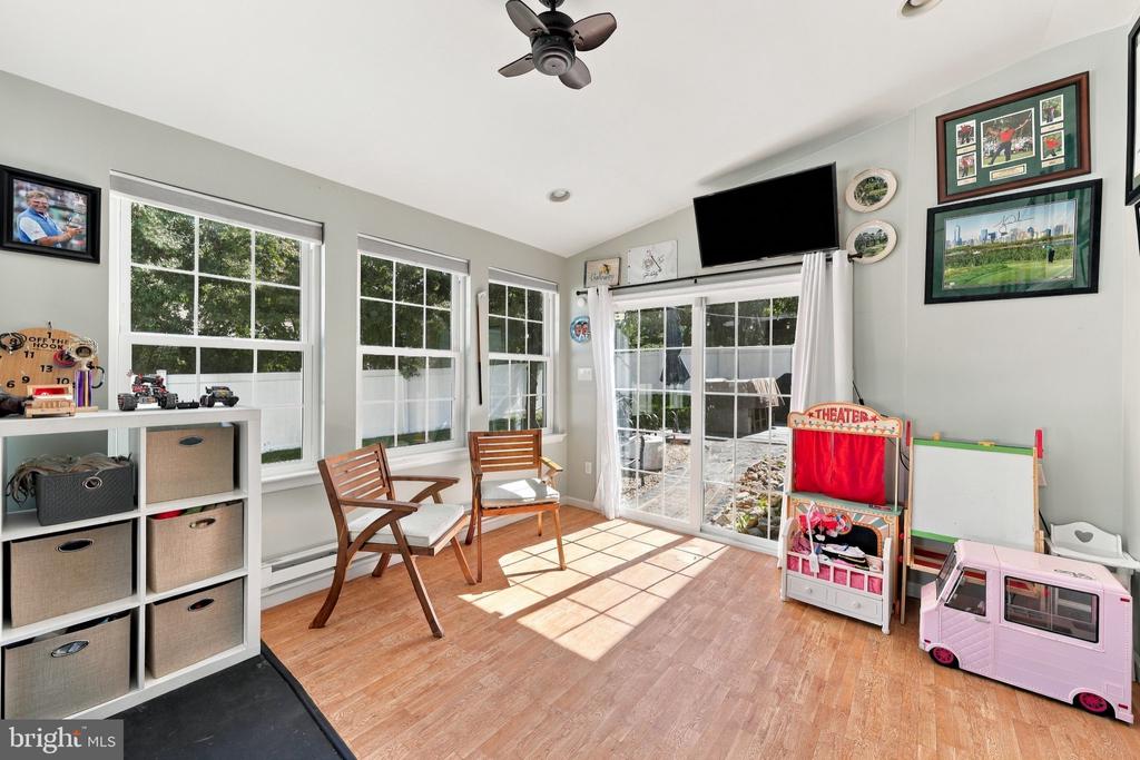 Bright sunroom with tall windows, sliding glass doors, wood floors, and children’s play furniture.