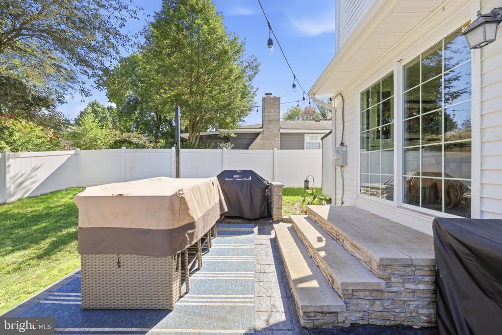 Backyard patio with covered wicker seating, stone steps, white fence, and string lights.