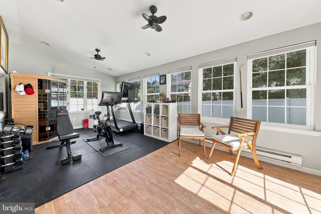Home gym with exercise equipment, large windows, and a sunlit seating area.