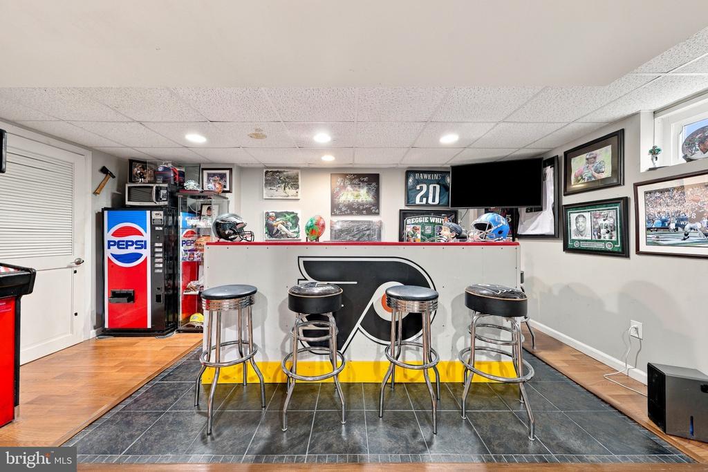 Basement sports bar with a counter, four stools, Eagles memorabilia, and a Pepsi vending machine.