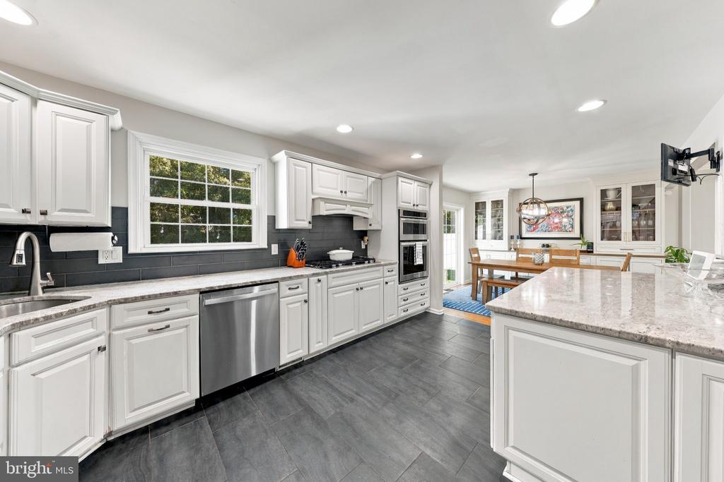 Bright kitchen with white cabinets, dark tile backsplash, stainless appliances, and a large marble island.