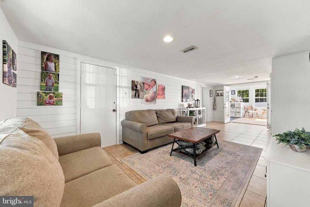 Living room with shiplap walls, neutral sofas, a patterned rug, and open doors to a sunlit dining area.