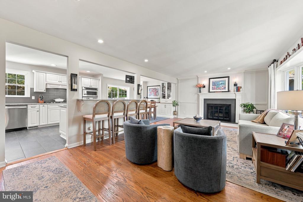 Open living and dining area with a fireplace, connected to a white kitchen by a breakfast bar.