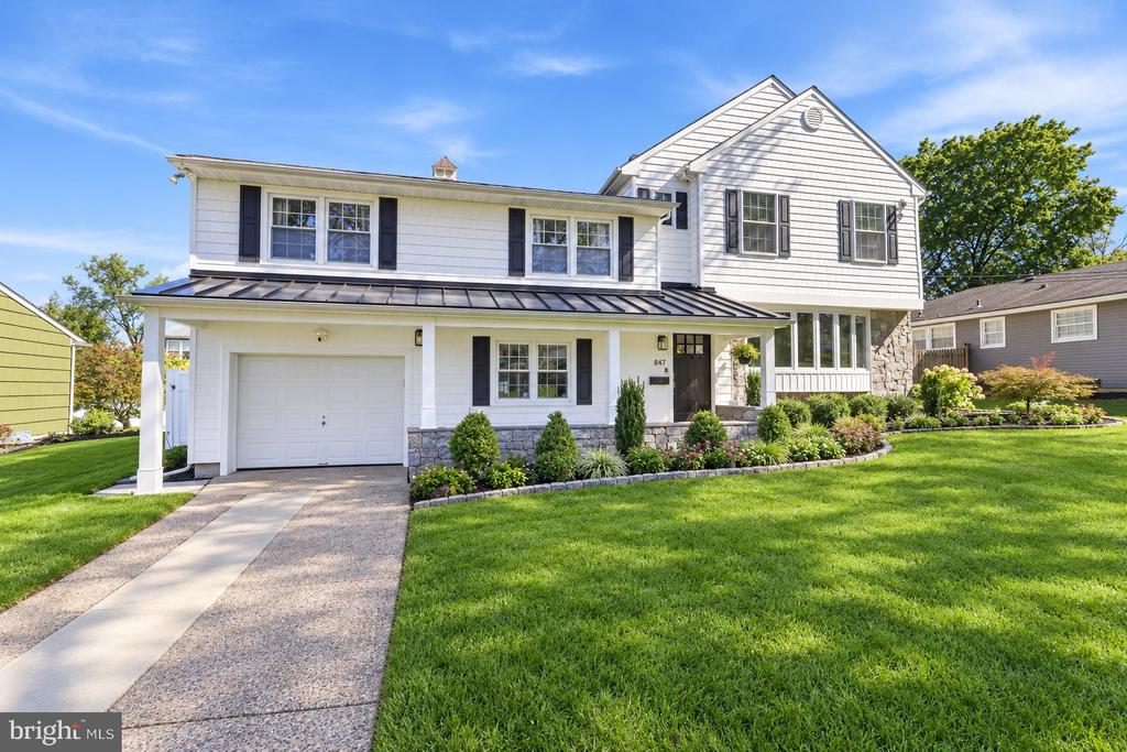 White two-story house with a stone façade, attached garage, landscaped flower beds, and a broad front lawn.