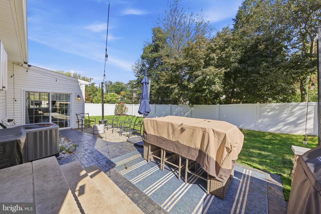 Fenced backyard patio with covered outdoor dining set, grill, and sliding glass doors.