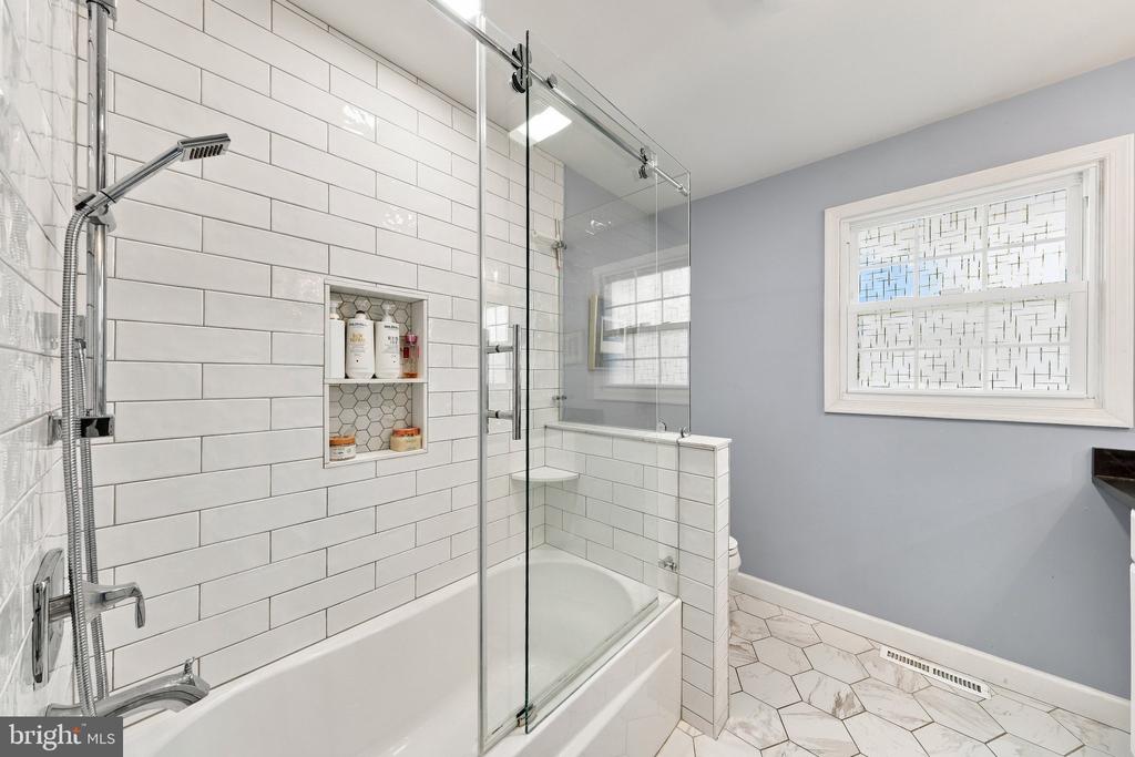 Bathroom with a glass-enclosed tub, white subway tile, and marble-look hexagonal flooring.