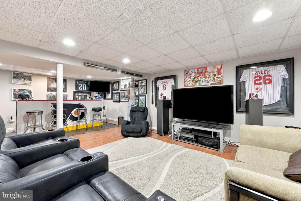 Furnished recreation room with a large TV, sports memorabilia, bar seating, and sofas.